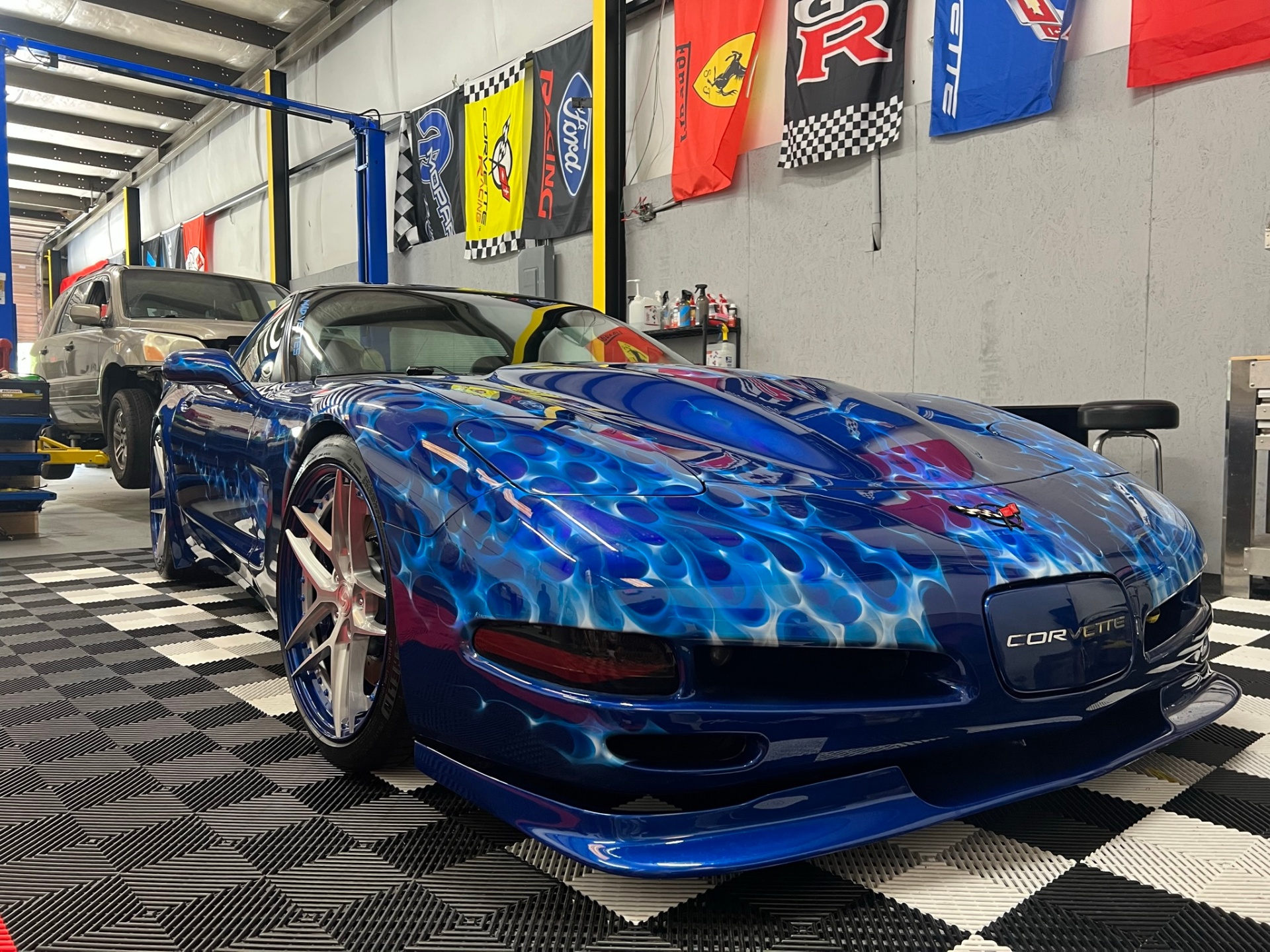 Blue custom Corvette with flame graphics inside the Phantom Auto Shield shop.