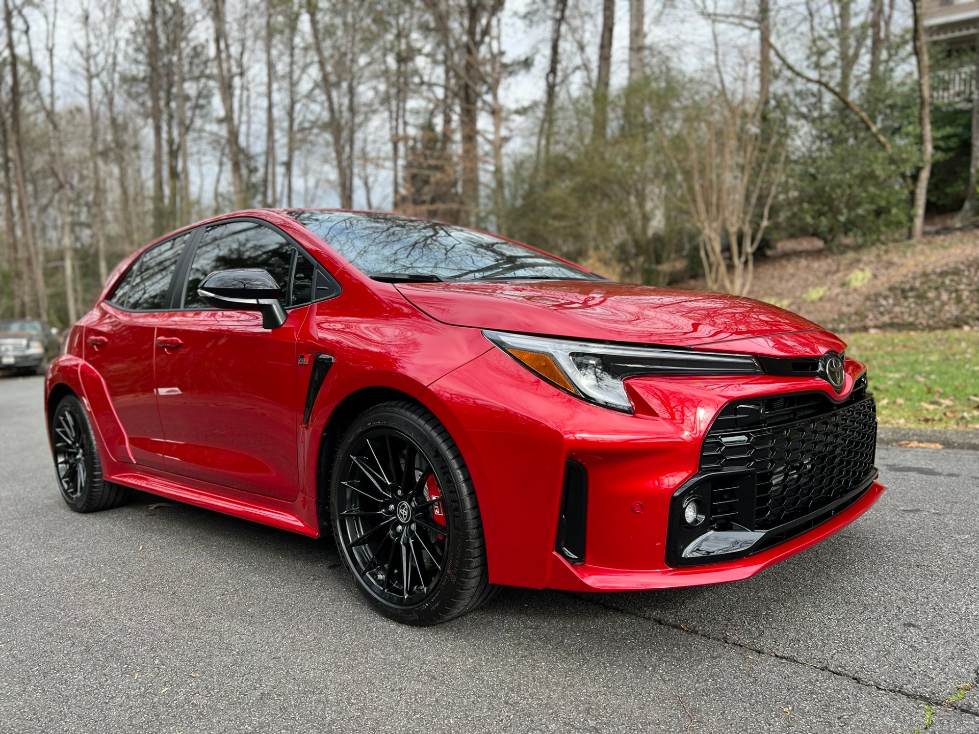 Red Toyota GR hot hatch with glossy finish on a cloudy day.